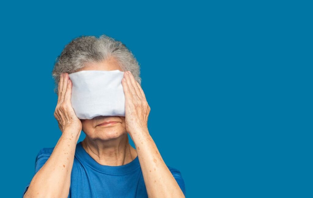 A senior with an eye stye gently presses a warm compress onto their eyes to help drain their eye stye and promote faster healing.