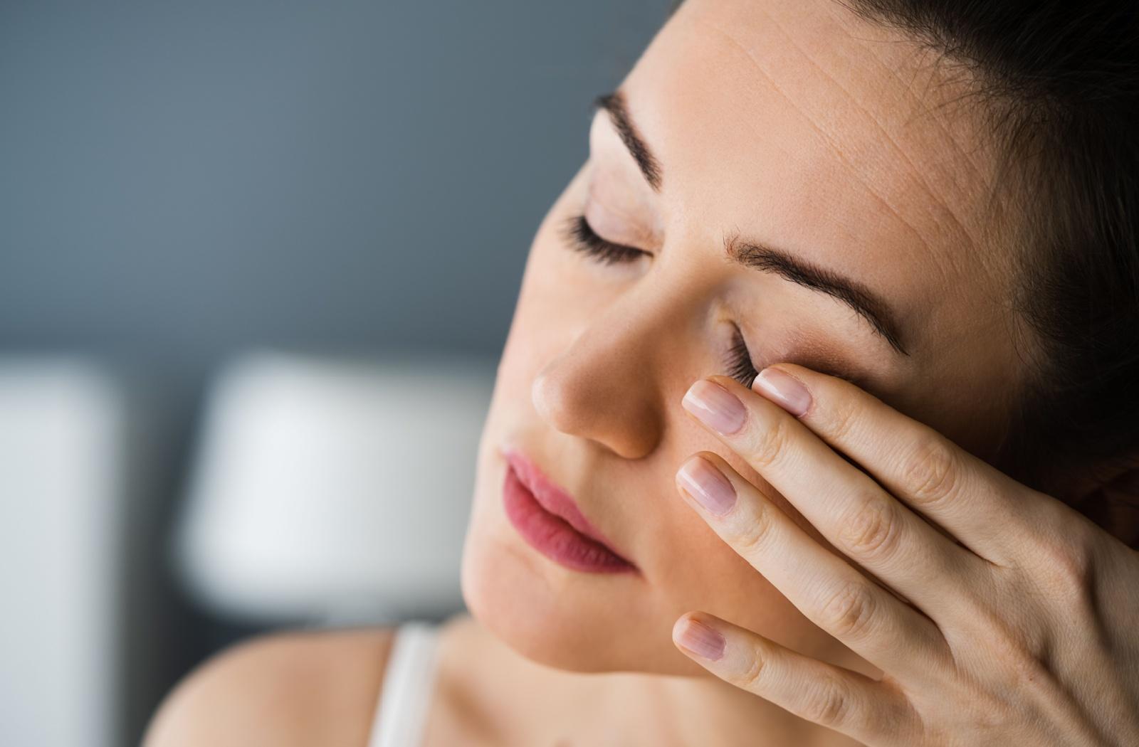 Woman gently touching her swollen eyelid, showing discomfort from eye irritation or inflammation.